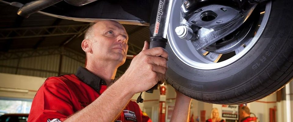 A Man In A Red Shirt Is Working On The Underside Of A Car — Hervey Bay Service Centre in Pialba, QLD