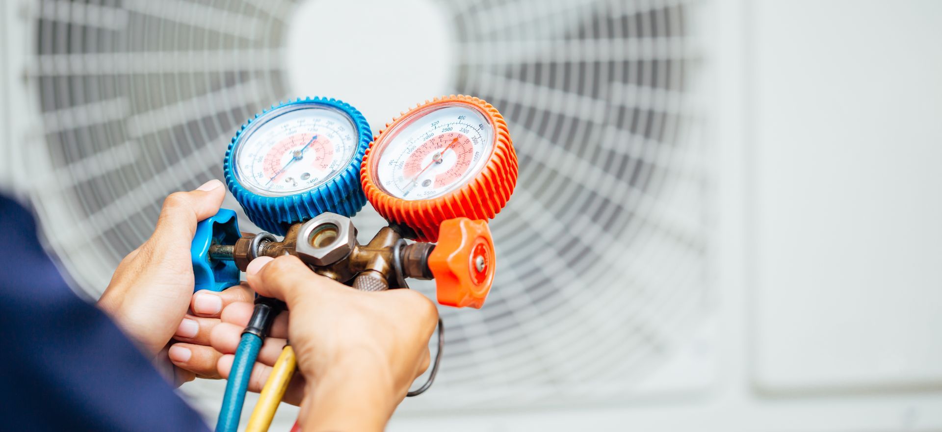 Hands holding gauges connected to an air conditioning unit.