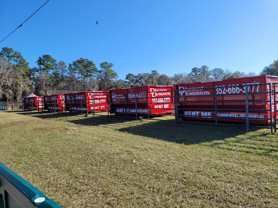 A row of red dumpsters are lined up in a grassy field.