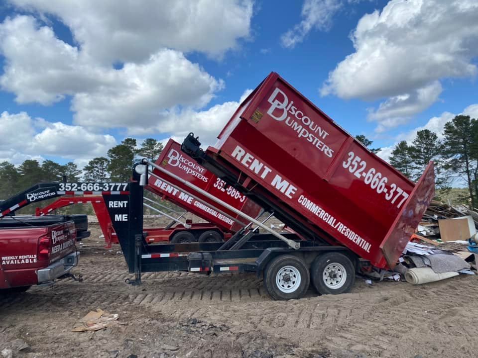 A dumpster is sitting on top of a trailer in a field.