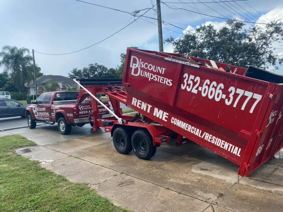 A red dumpster is being pulled by a truck on a trailer.