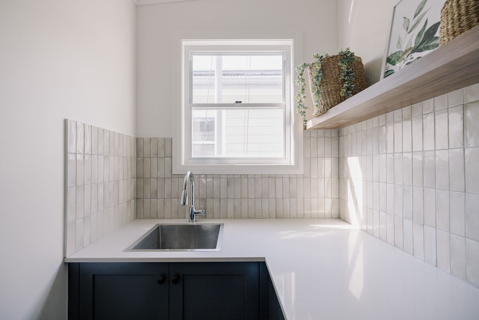 Laundry room with a sink, blue cabinets, white counter and tile backsplash, and window.