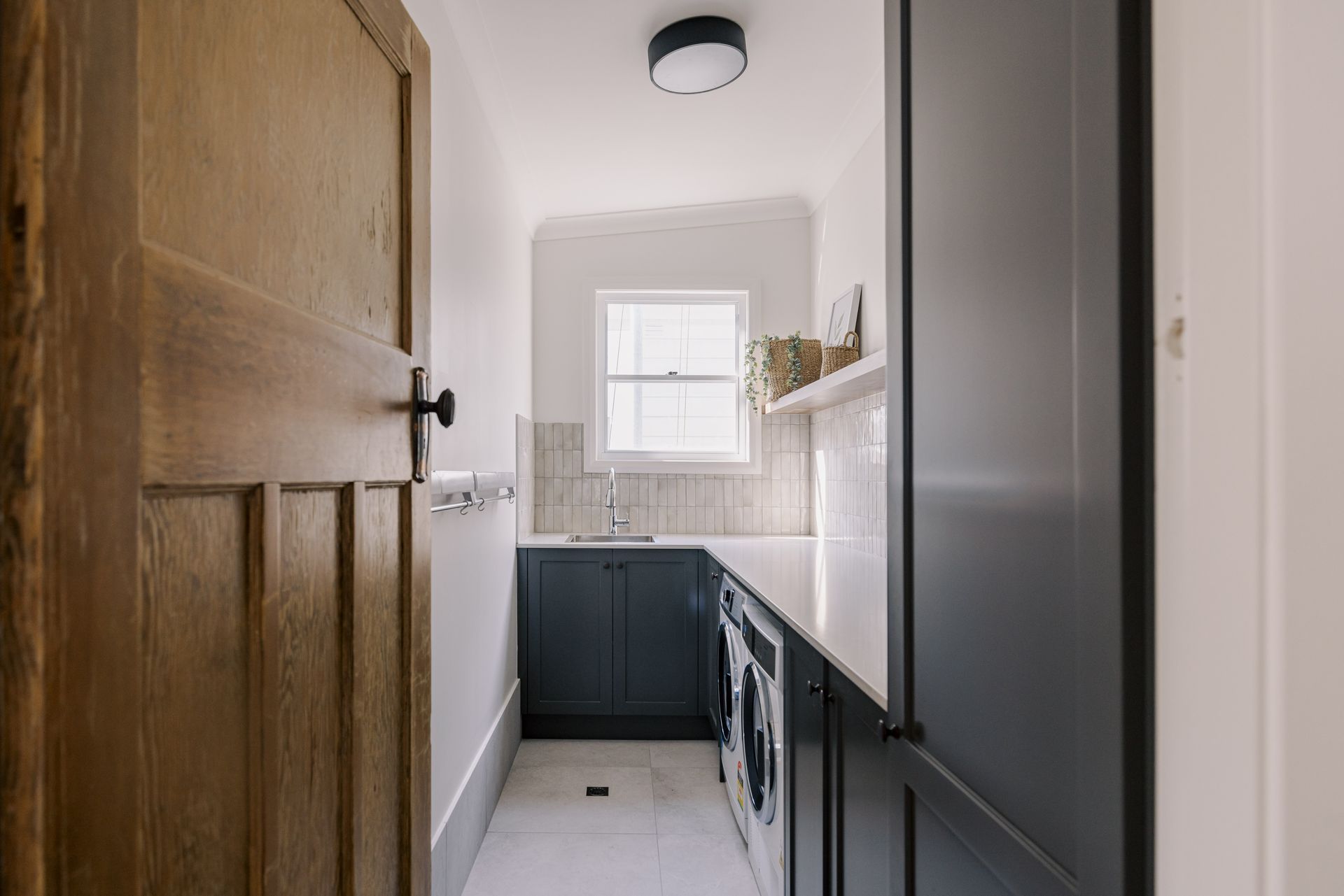 Laundry room with wooden door, navy cabinets, white countertops, and window.