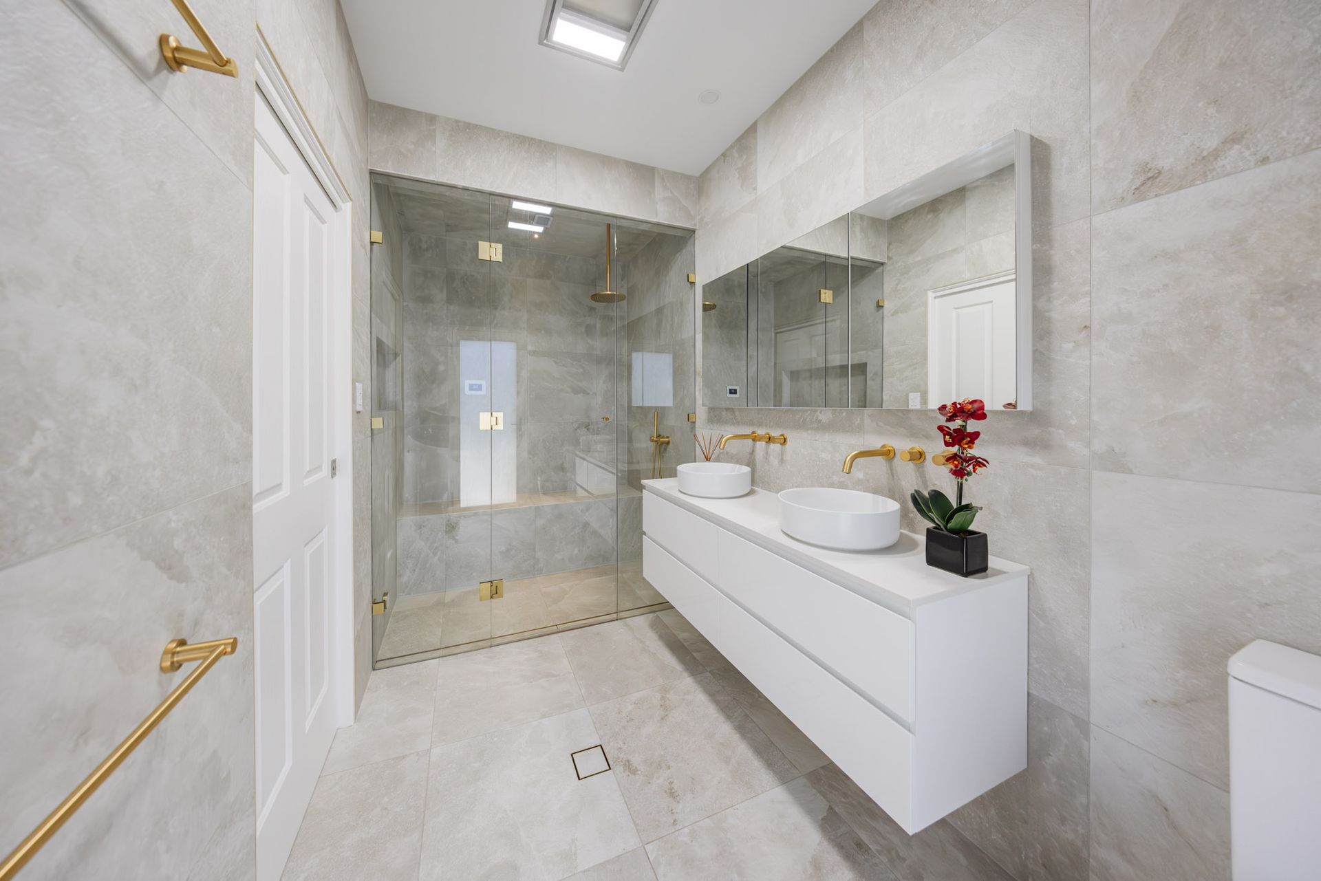 Modern bathroom with white floating vanity, gold fixtures, large mirror, and glass shower.