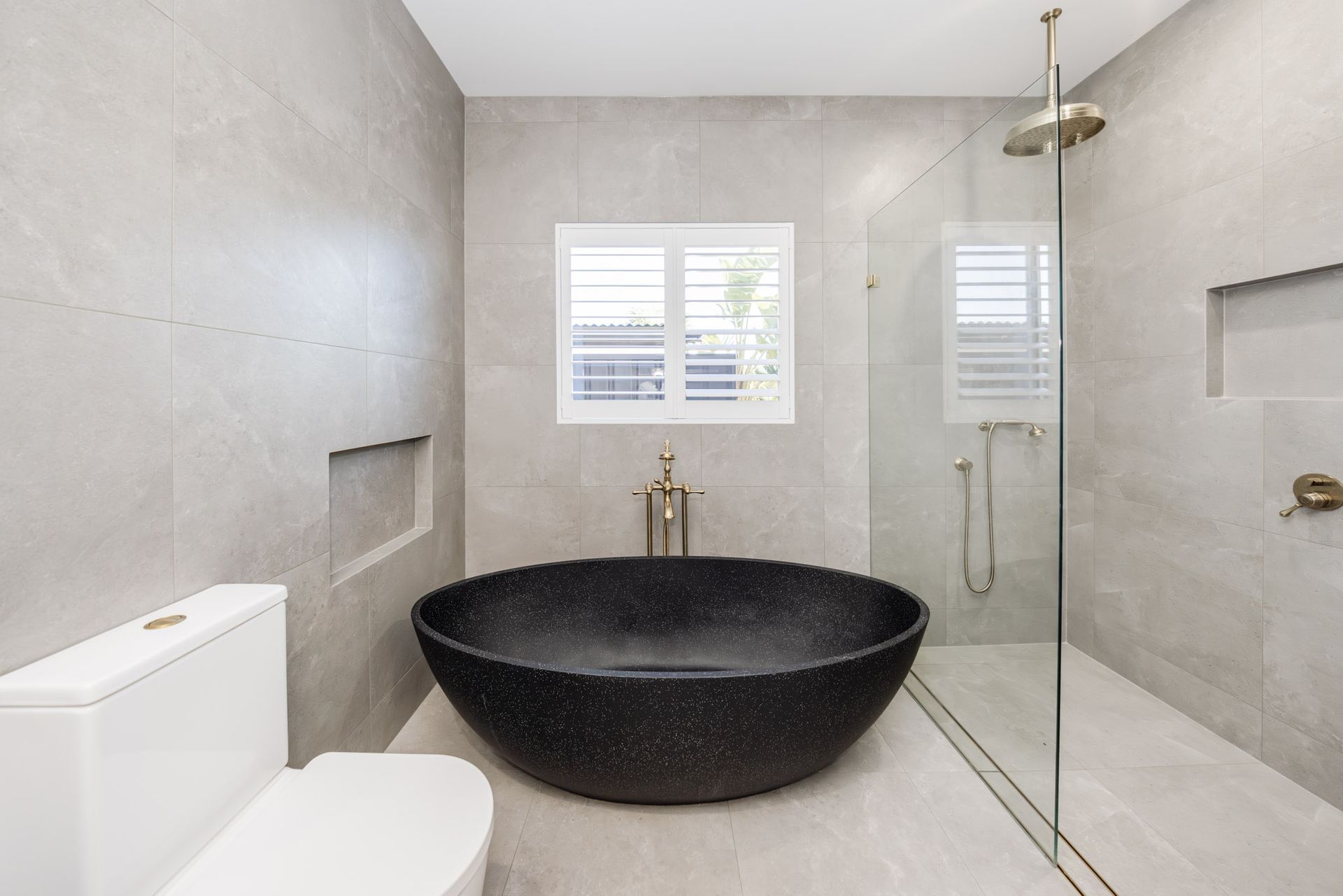 Modern bathroom with black tub, glass shower, gray tile, and white toilet.
