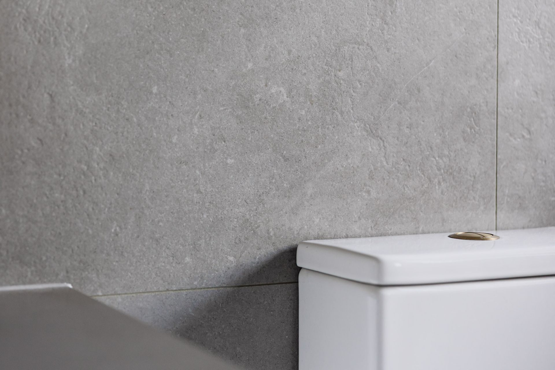 Gray tiled wall above a white toilet.
