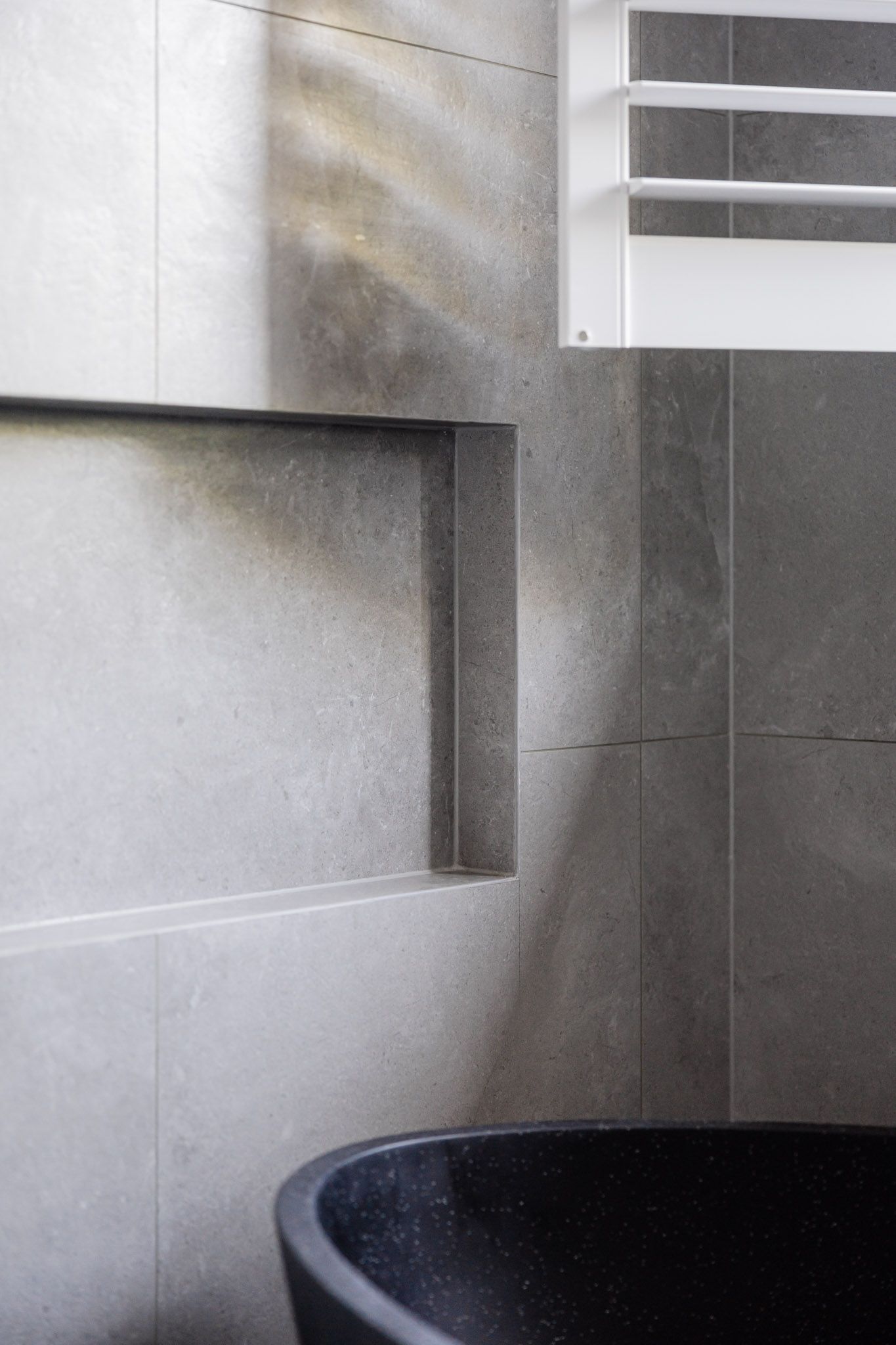 Modern bathroom with gray tile walls, a black tub, and built-in shelves.