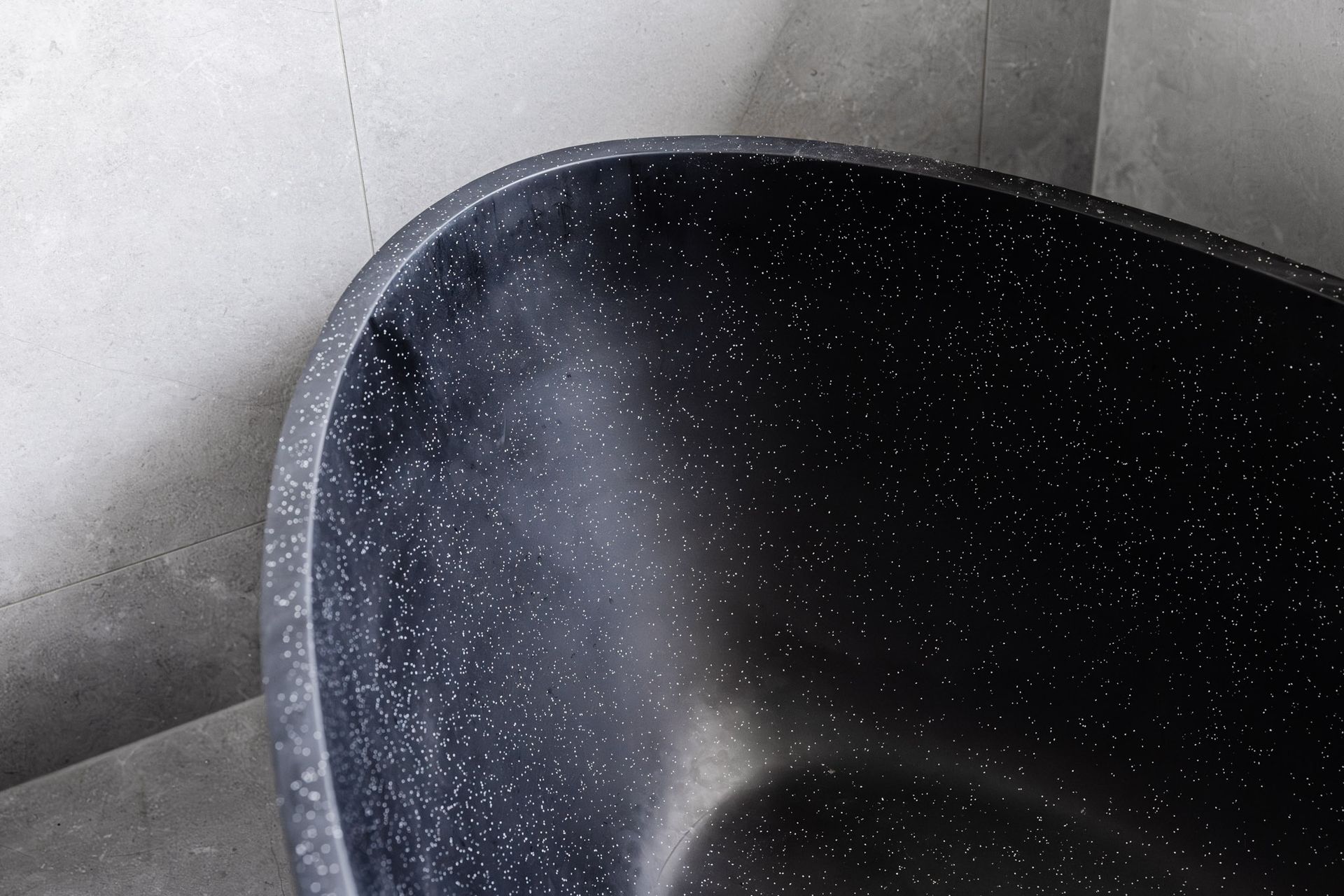 Black speckled bathtub against a gray concrete wall.