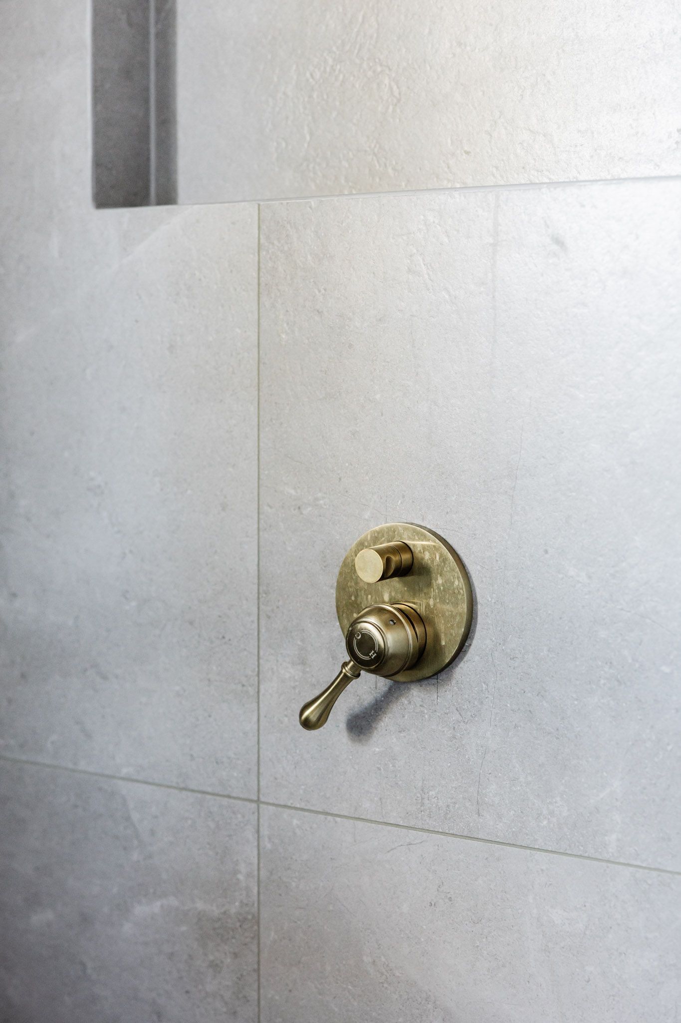 Brass shower control on a light gray tiled wall.