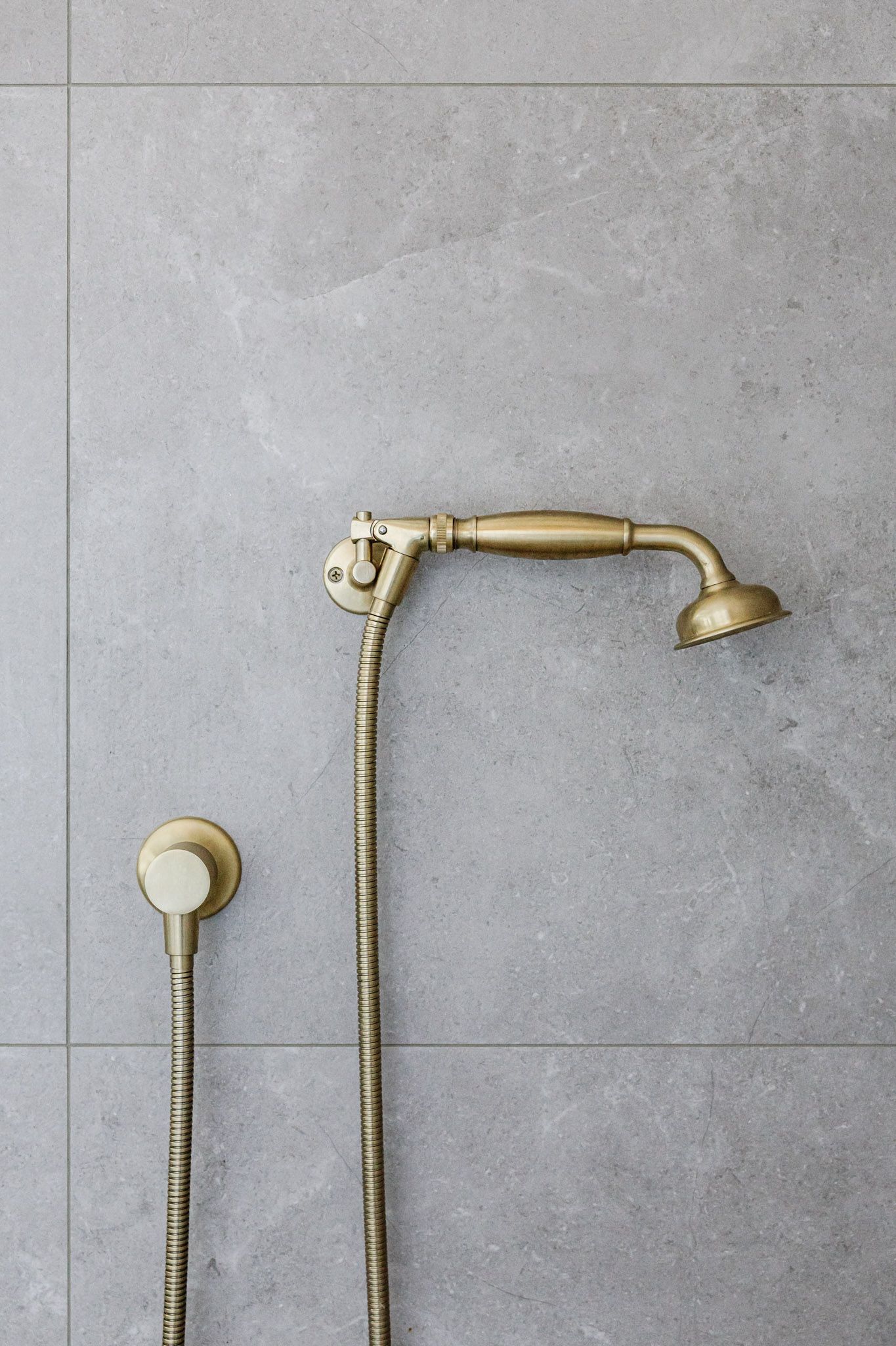Gold-toned shower fixtures against gray tile wall. Handheld sprayer and overhead shower head with vintage design.