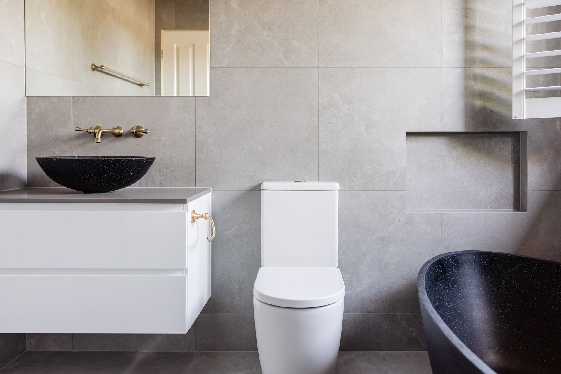 Modern bathroom with grey tile walls, white vanity, black sink and tub, and white toilet.