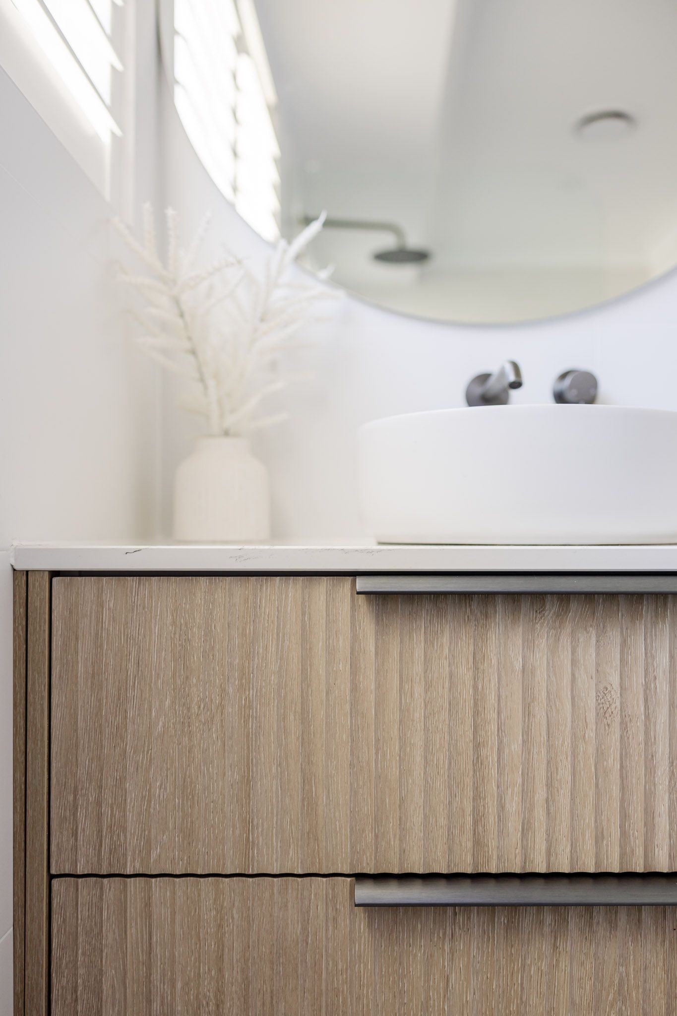 Wooden bathroom vanity with two drawers, white countertop, round mirror, and sink.