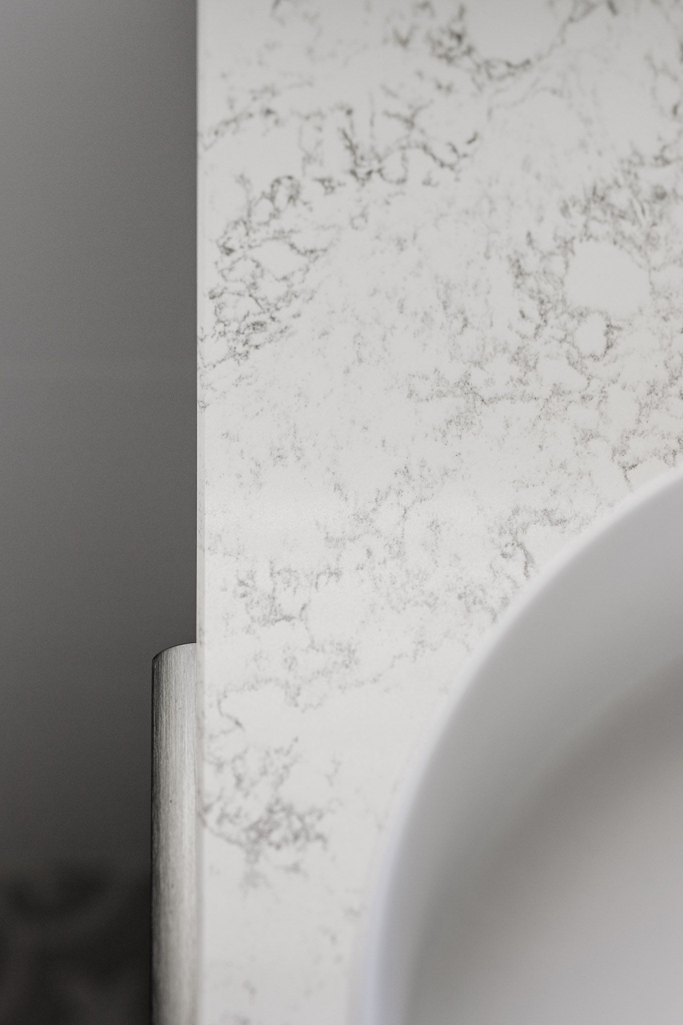 White marble countertop with gray veining next to a white sink basin and a gray wall.