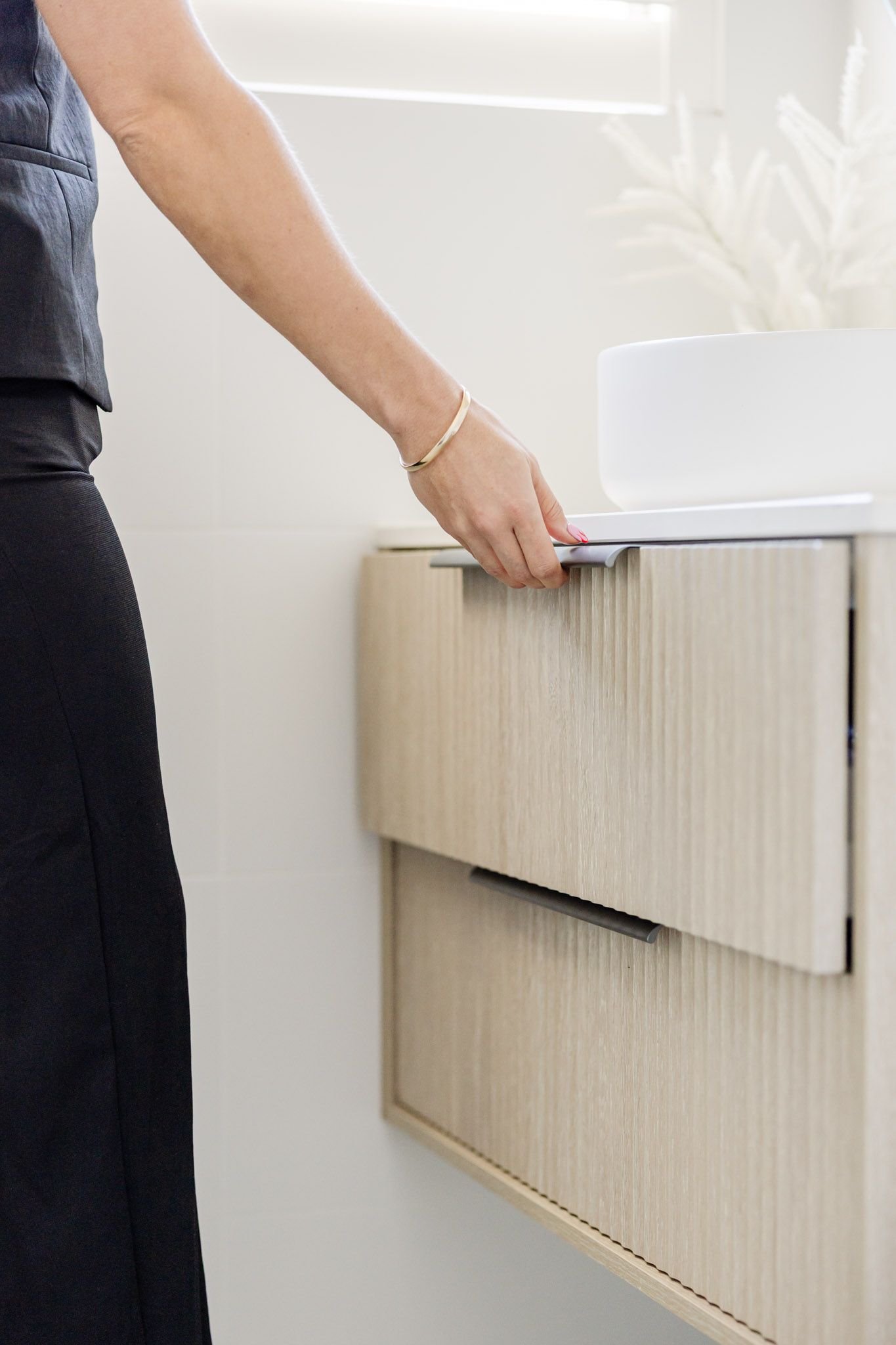 Woman opening a light wood bathroom drawer. White walls, modern sink.