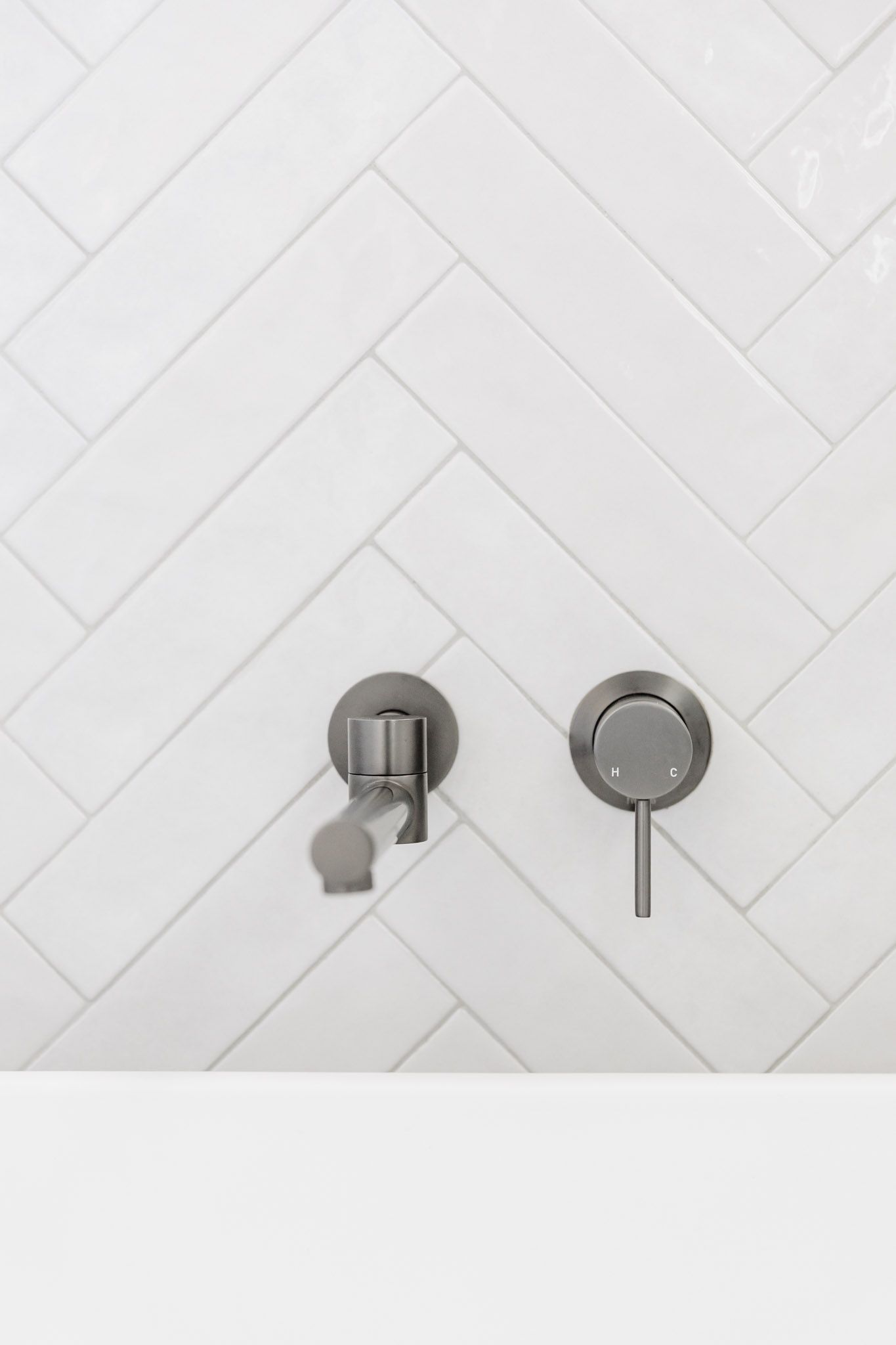 Brushed nickel shower fixtures on white herringbone tile, next to a white surface.