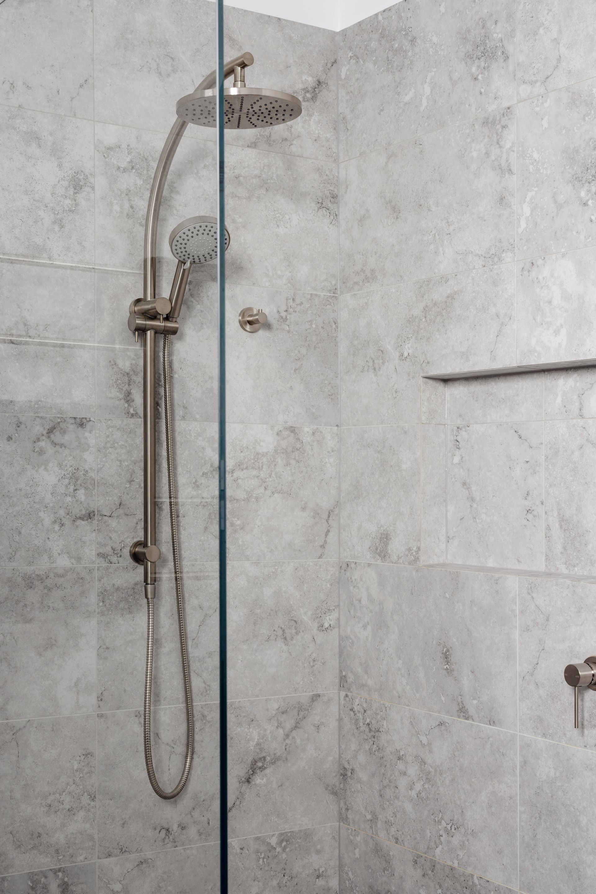Shower stall with gray textured tiles, silver shower head and fixtures behind glass panel.