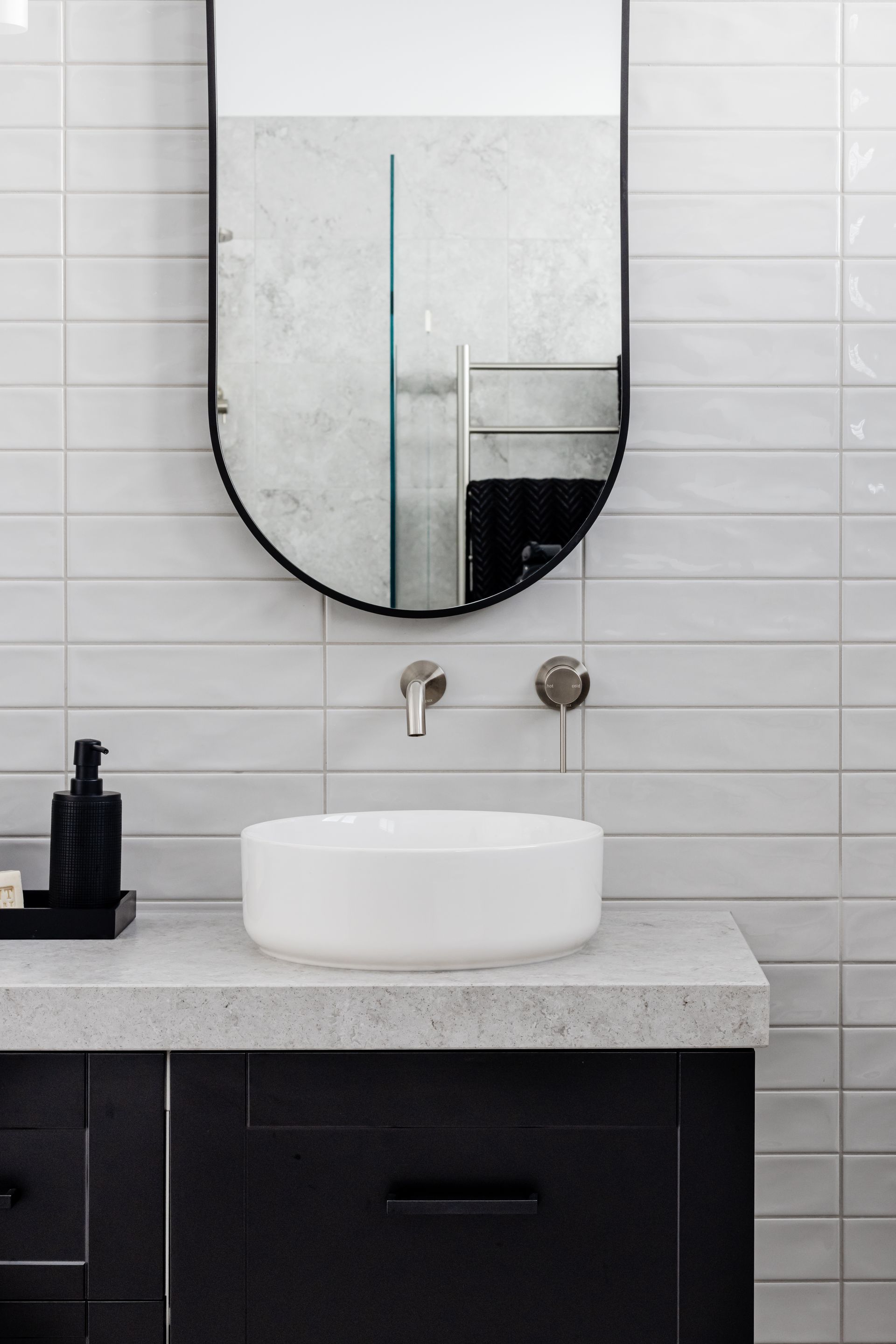Bathroom with black vanity, white countertop, oval mirror, and round sink.