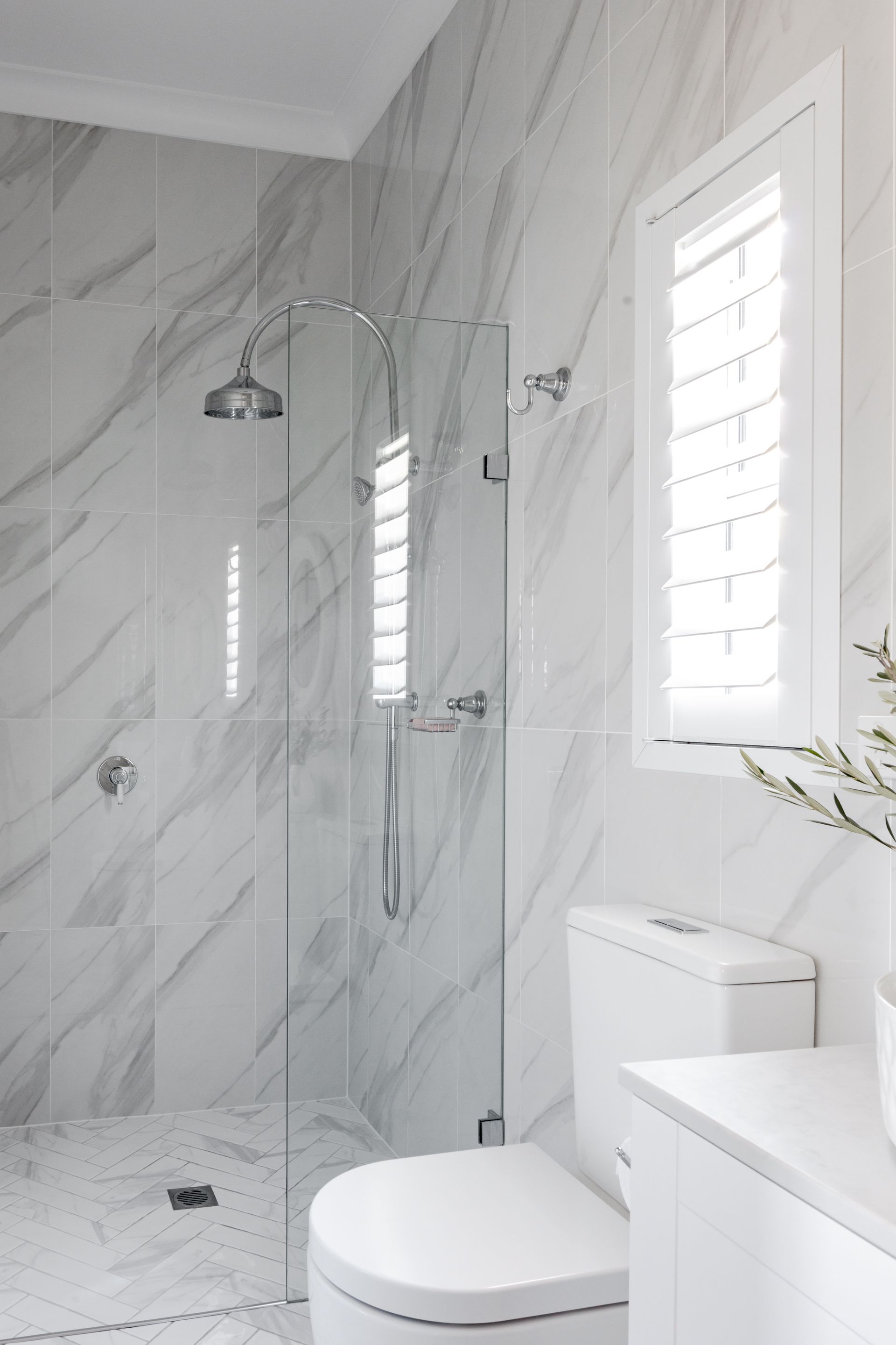 Elegant white marble bathroom with shower, toilet, and shuttered window.