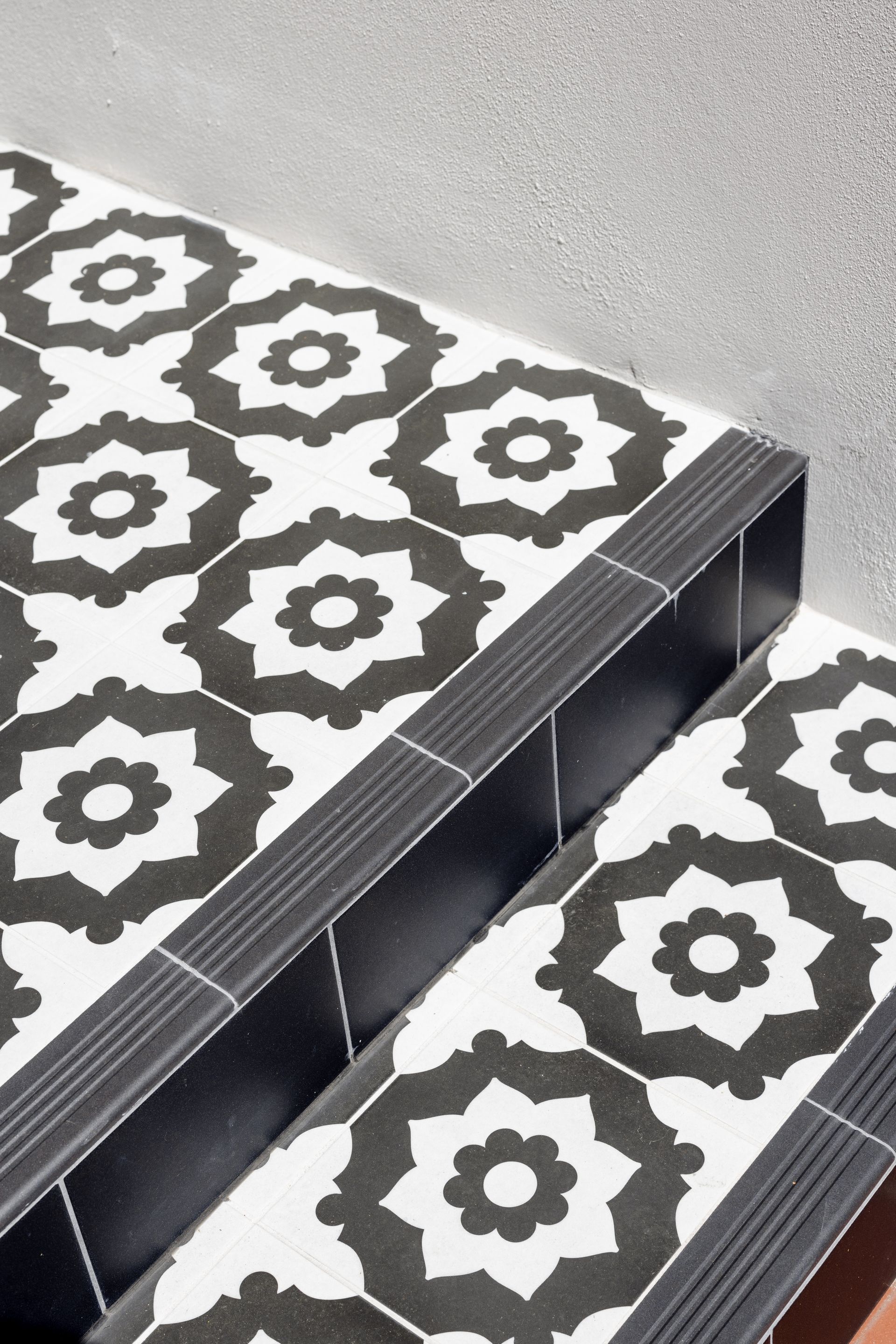 Steps with black and white floral tile pattern, dark trim, and a white wall.