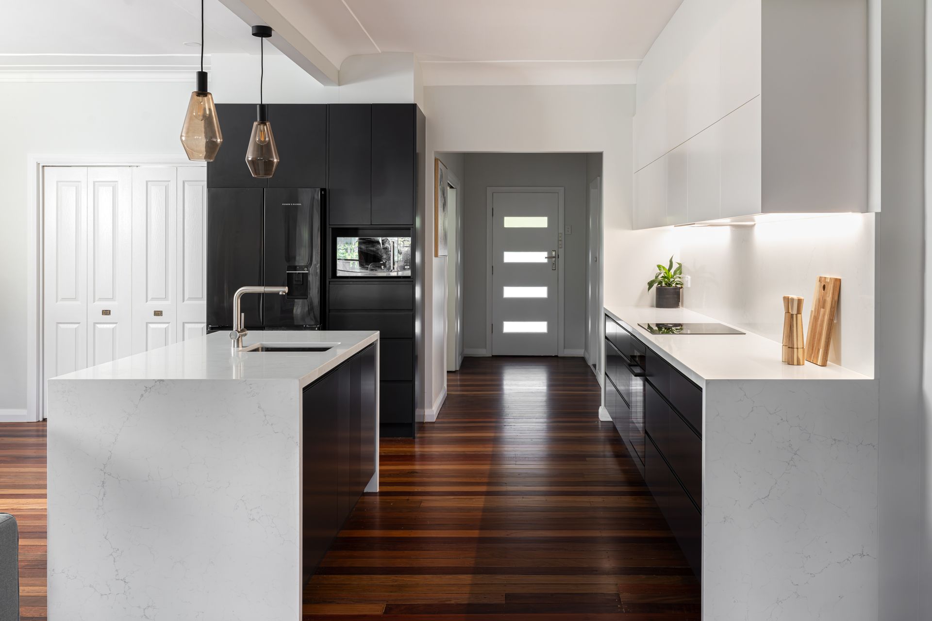 Modern kitchen with white countertops, dark cabinets, and wood flooring.