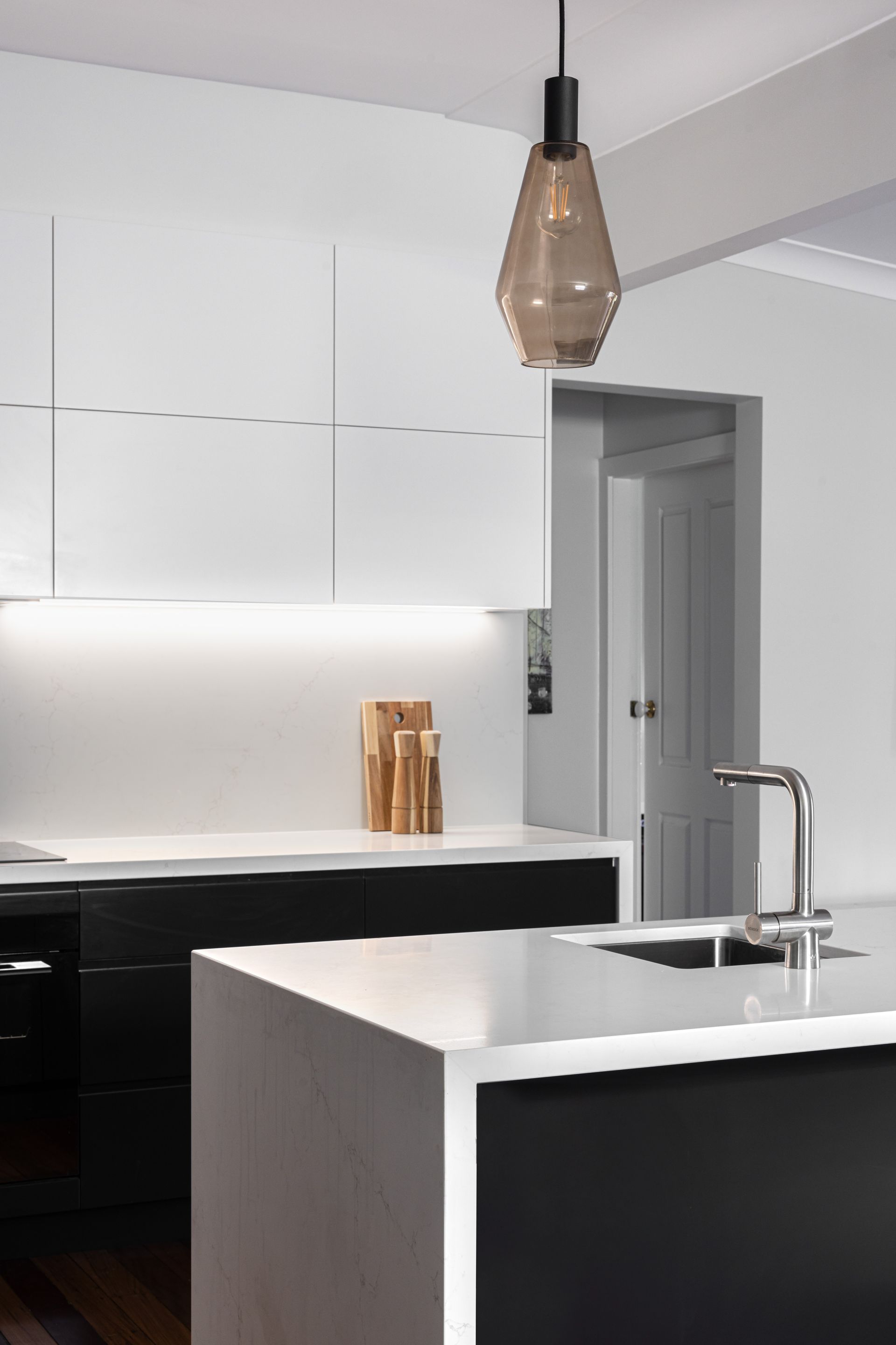 Modern kitchen with black and white cabinets, quartz countertops, and a pendant light.