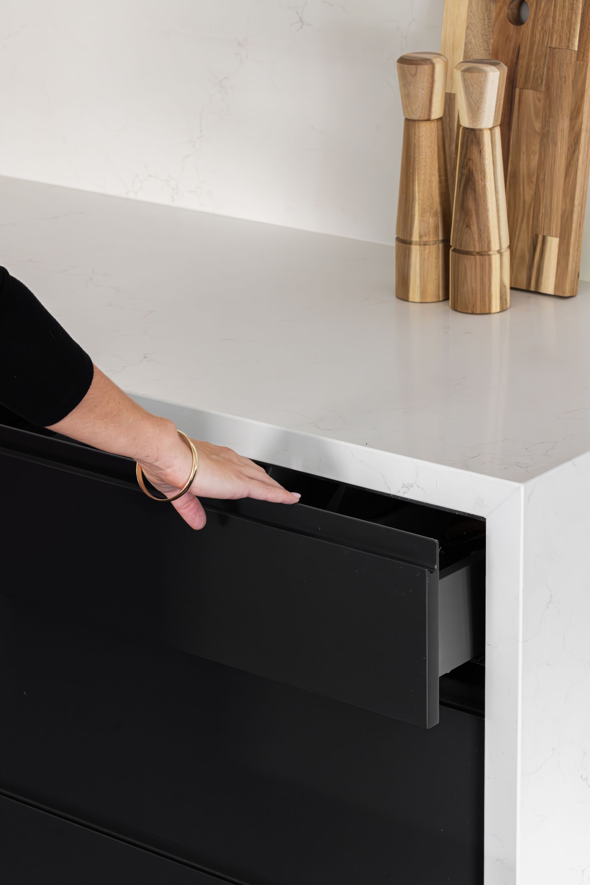 A person opens a black kitchen drawer on a white countertop.