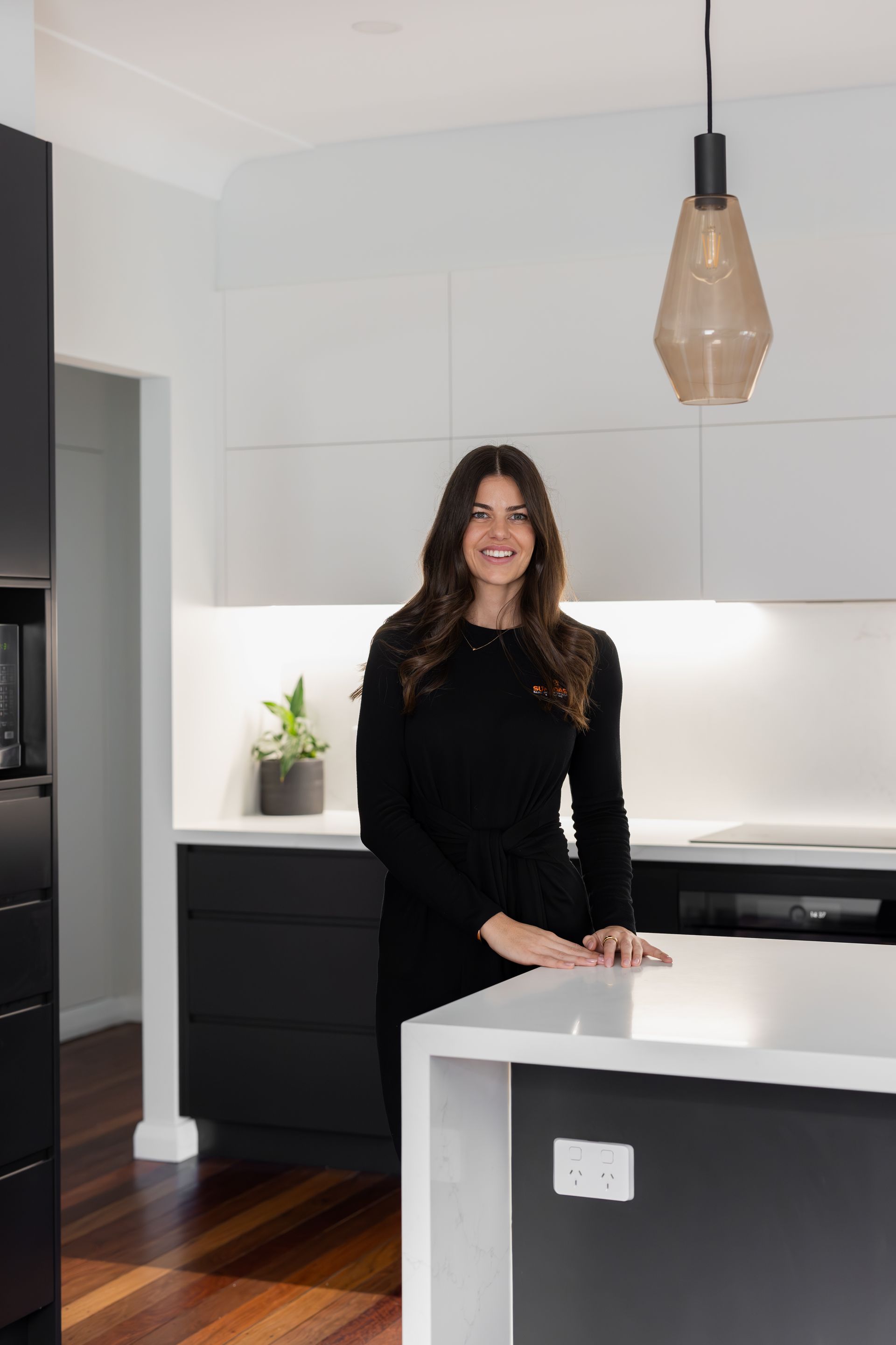 Woman in black dress smiles in a modern black and white kitchen.