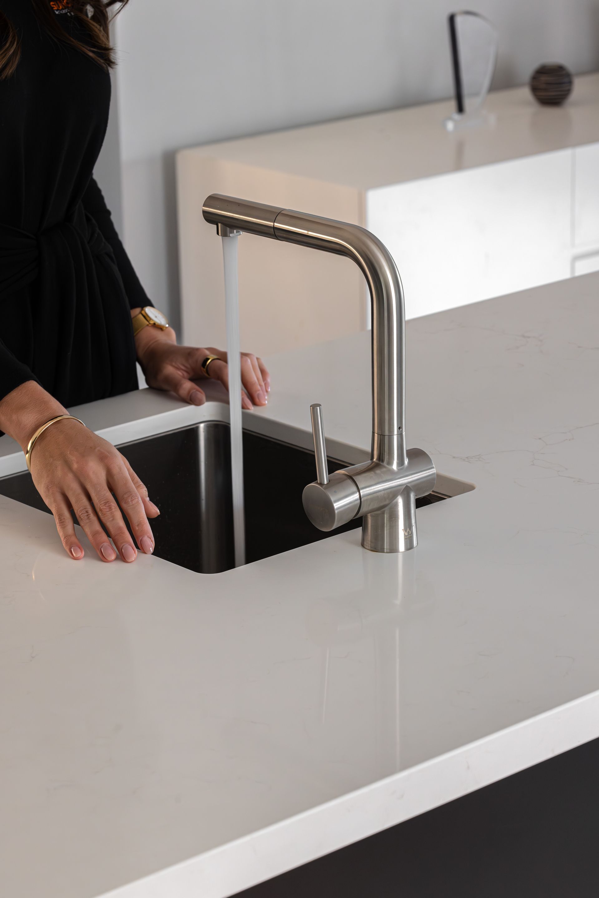 Person using a modern, brushed-nickel faucet to fill a dark sink, set in a white countertop.