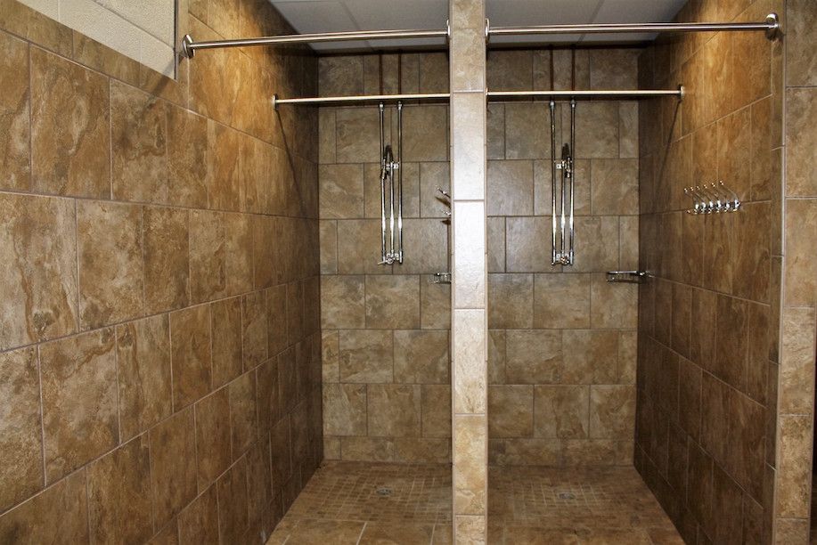 Two tiled shower stalls with metal showerheads and curtain rods.