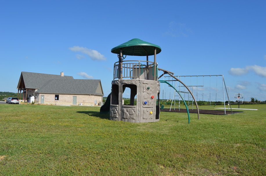 Playground with climbing tower, slide, swings, and building in the background on a sunny day.