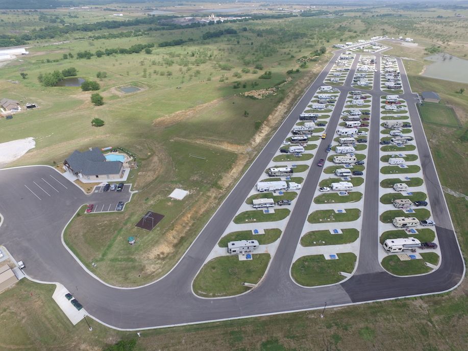 Aerial view of an RV park with numerous RVs parked on paved lots, a clubhouse, and surrounding green space.