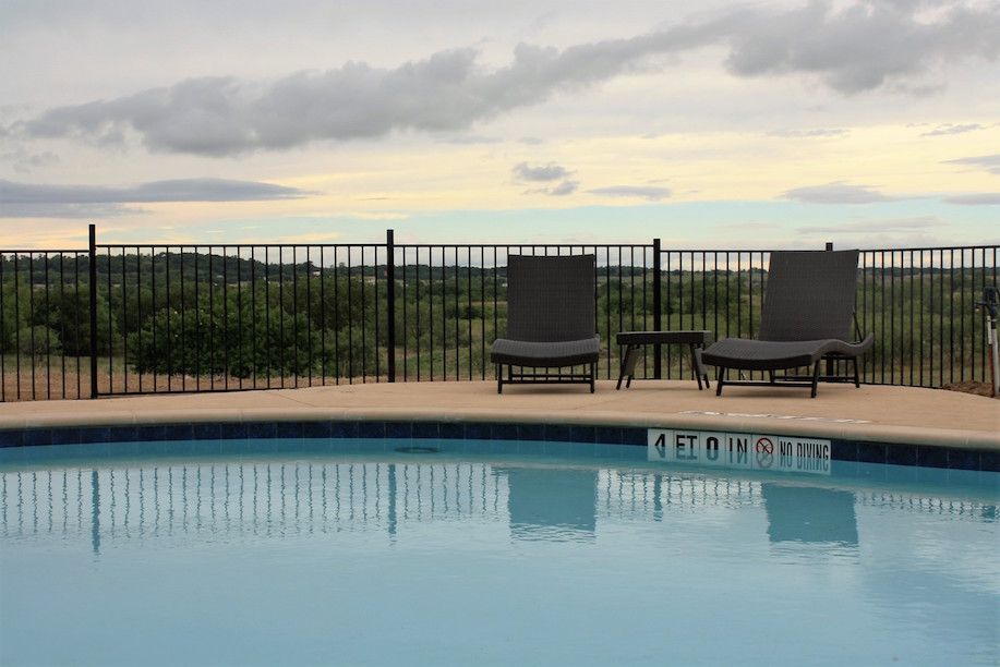Swimming pool with two lounge chairs overlooking a landscape under a cloudy sky.