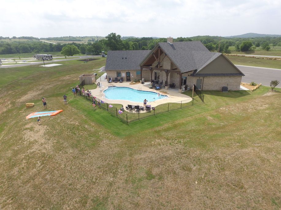House with pool, people, grassy yard. Paraglider in field. Sunny day.