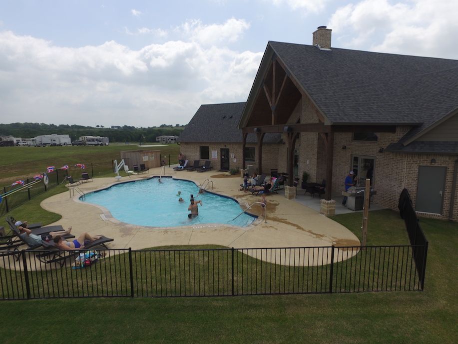 A house with a pool in the backyard with people swimming. Lounge chairs and a fence are around the pool.