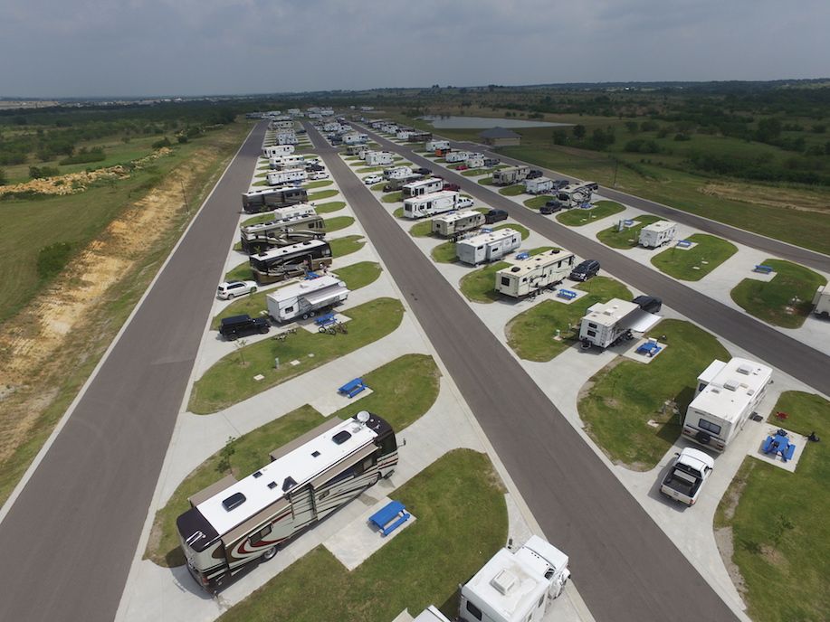 Aerial view of an RV park with numerous RVs parked on paved lots with grass dividers, under a cloudy sky.