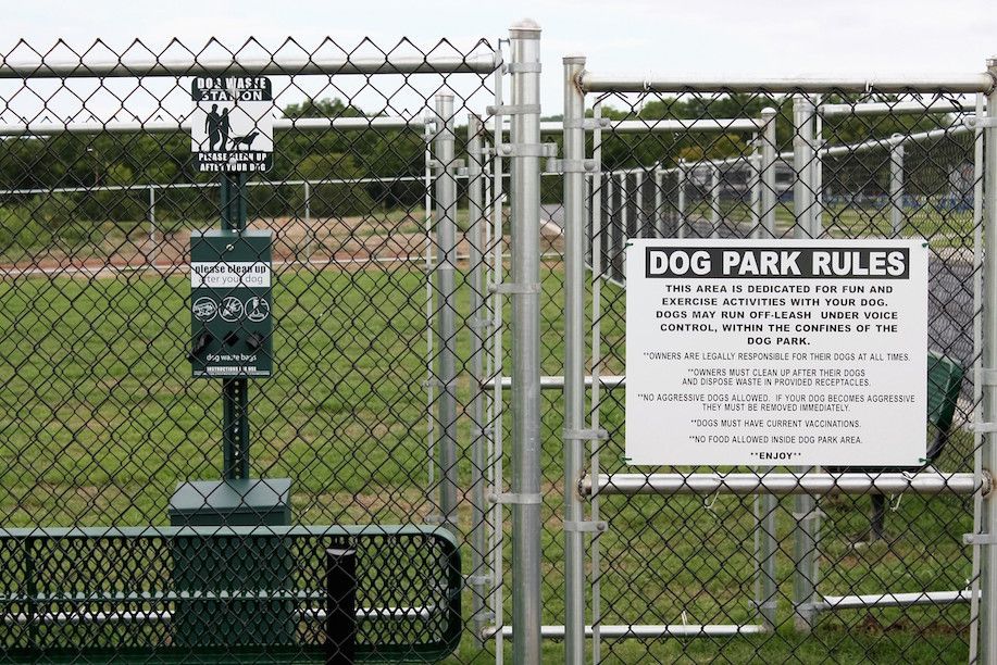 Chain link fence gate to a dog park with rules sign and waste bag dispenser.