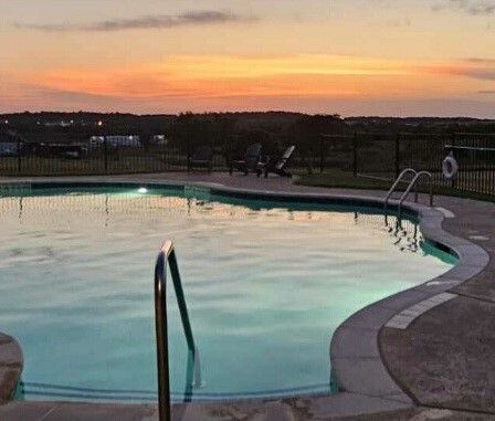 Pool at dusk with orange and yellow sky, black fence, and lounge chairs.