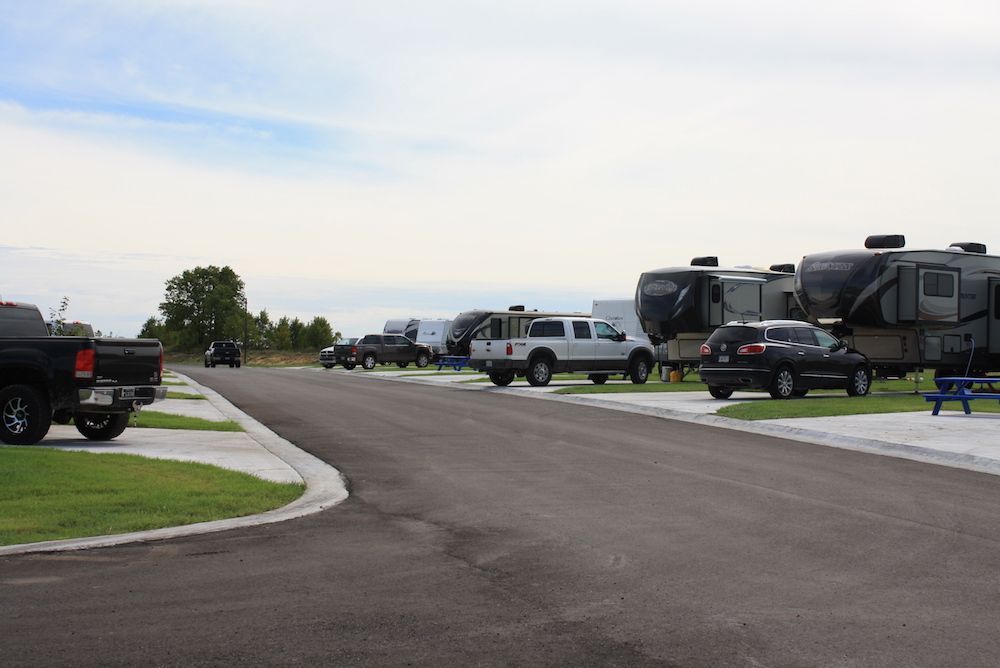 Campground road with RVs, trucks, and a golf cart parked on gravel sites.