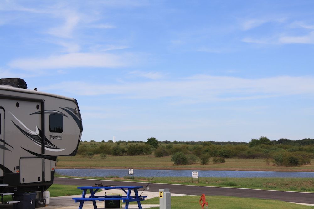 RV parked by a lake, blue picnic table, green grass, blue sky.