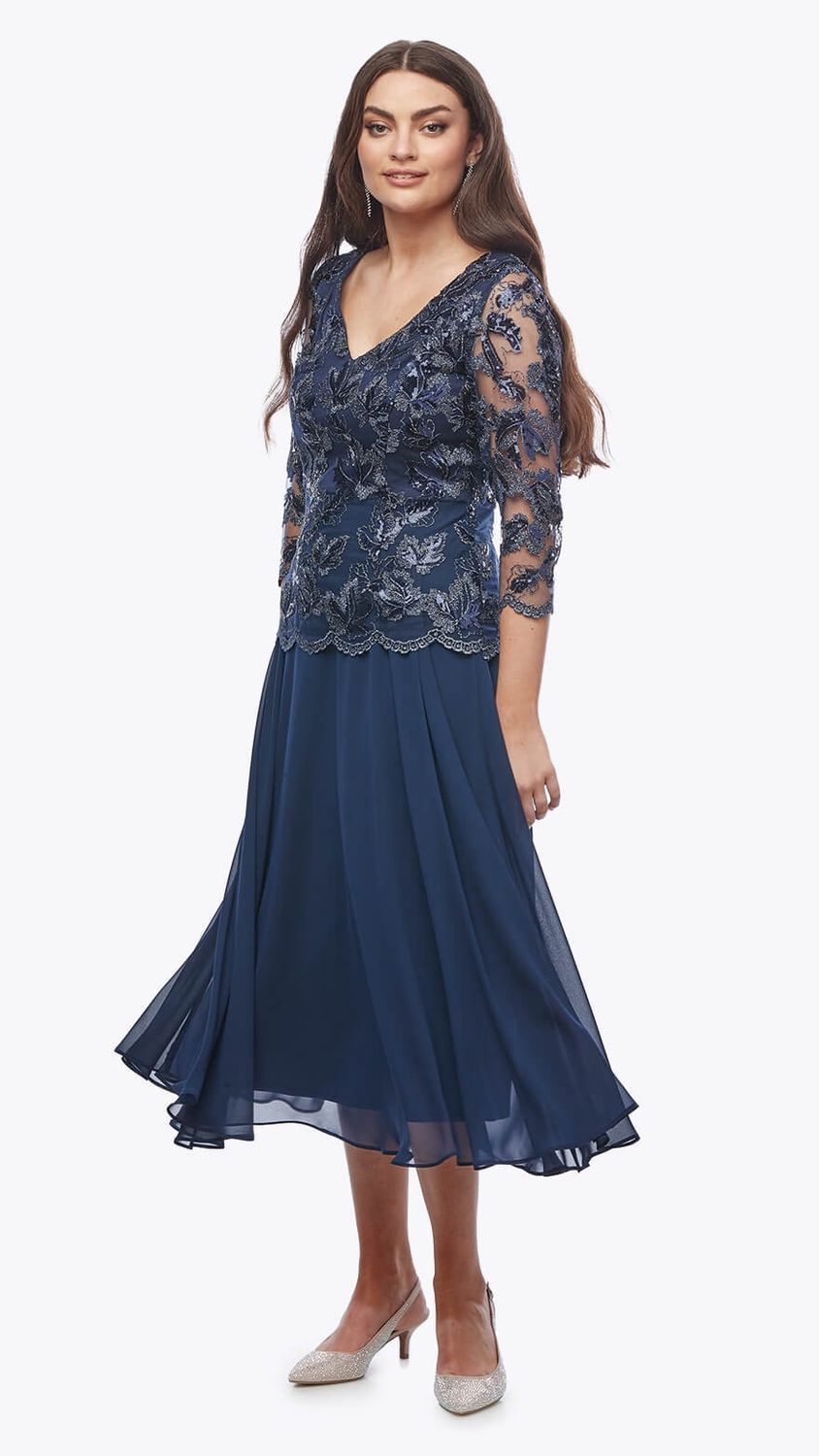 Woman in a navy blue formal dress with beaded bodice, three-quarter sleeves, and midi skirt, smiling.