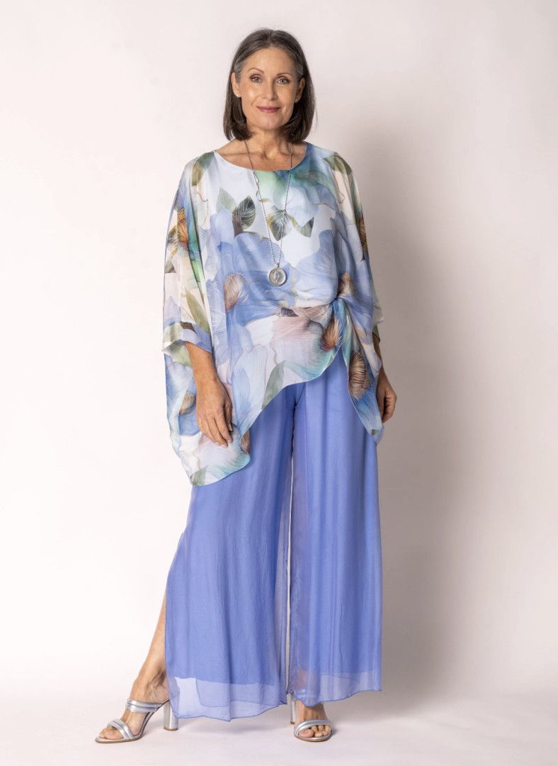 Woman in blue patterned top and pants, standing.