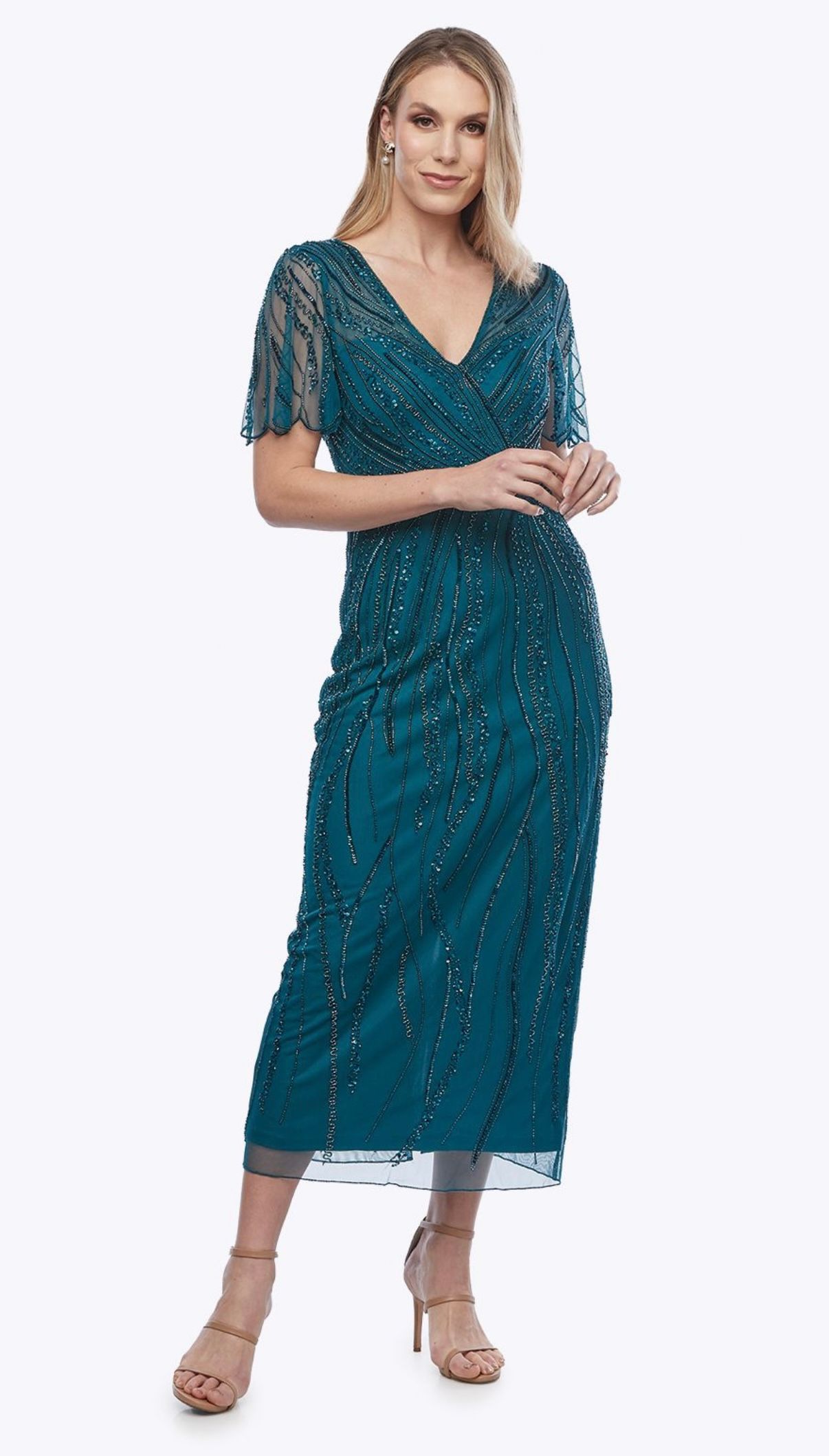 Woman in teal beaded dress and nude heels, standing against a white background.