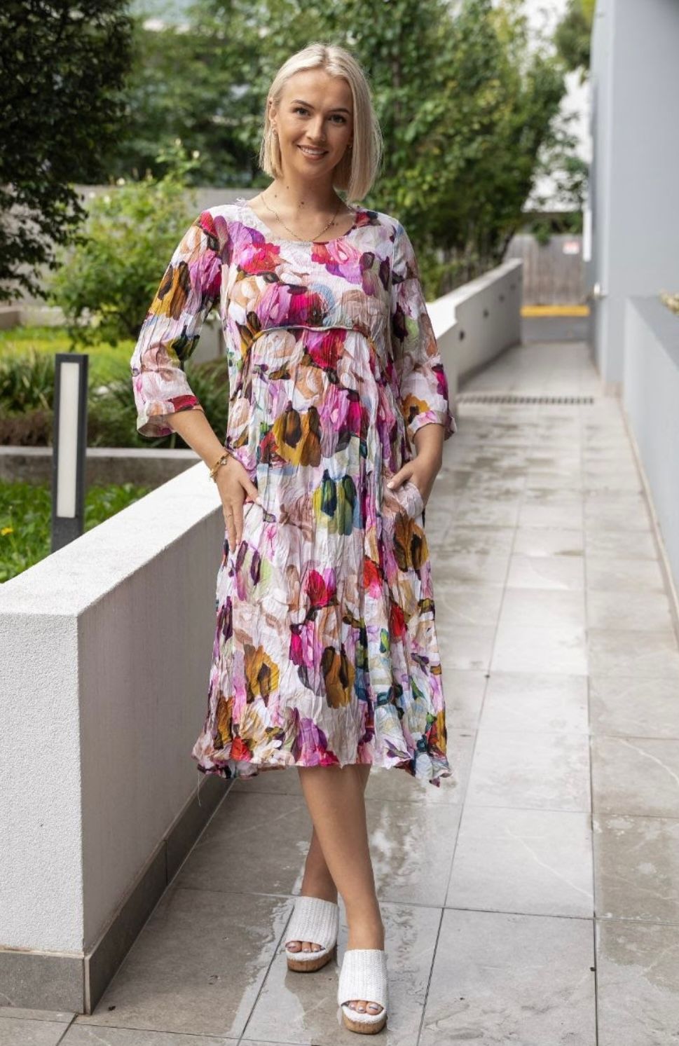 A woman in a floral dress is standing on a sidewalk.