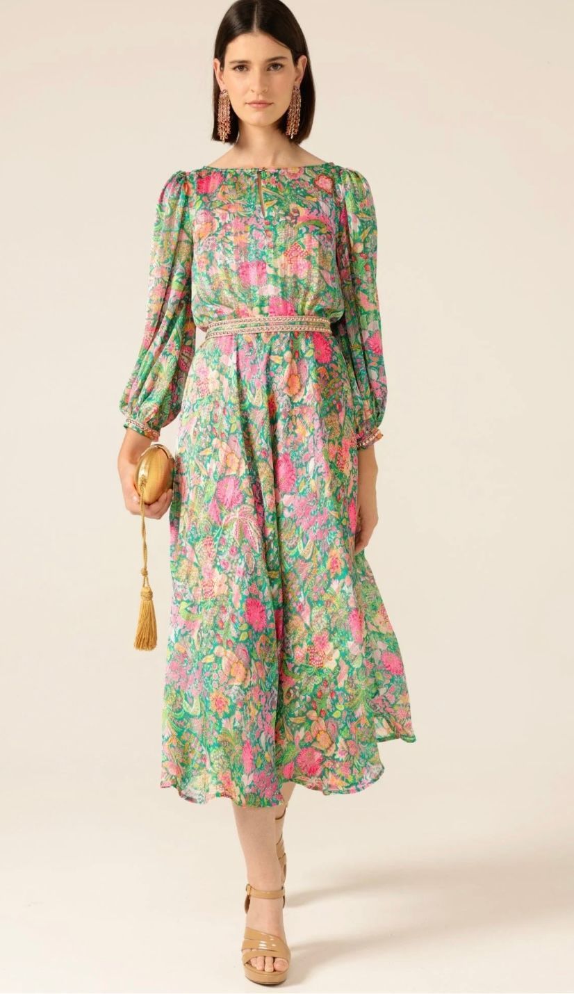 A woman is wearing a green floral dress and holding a clutch.