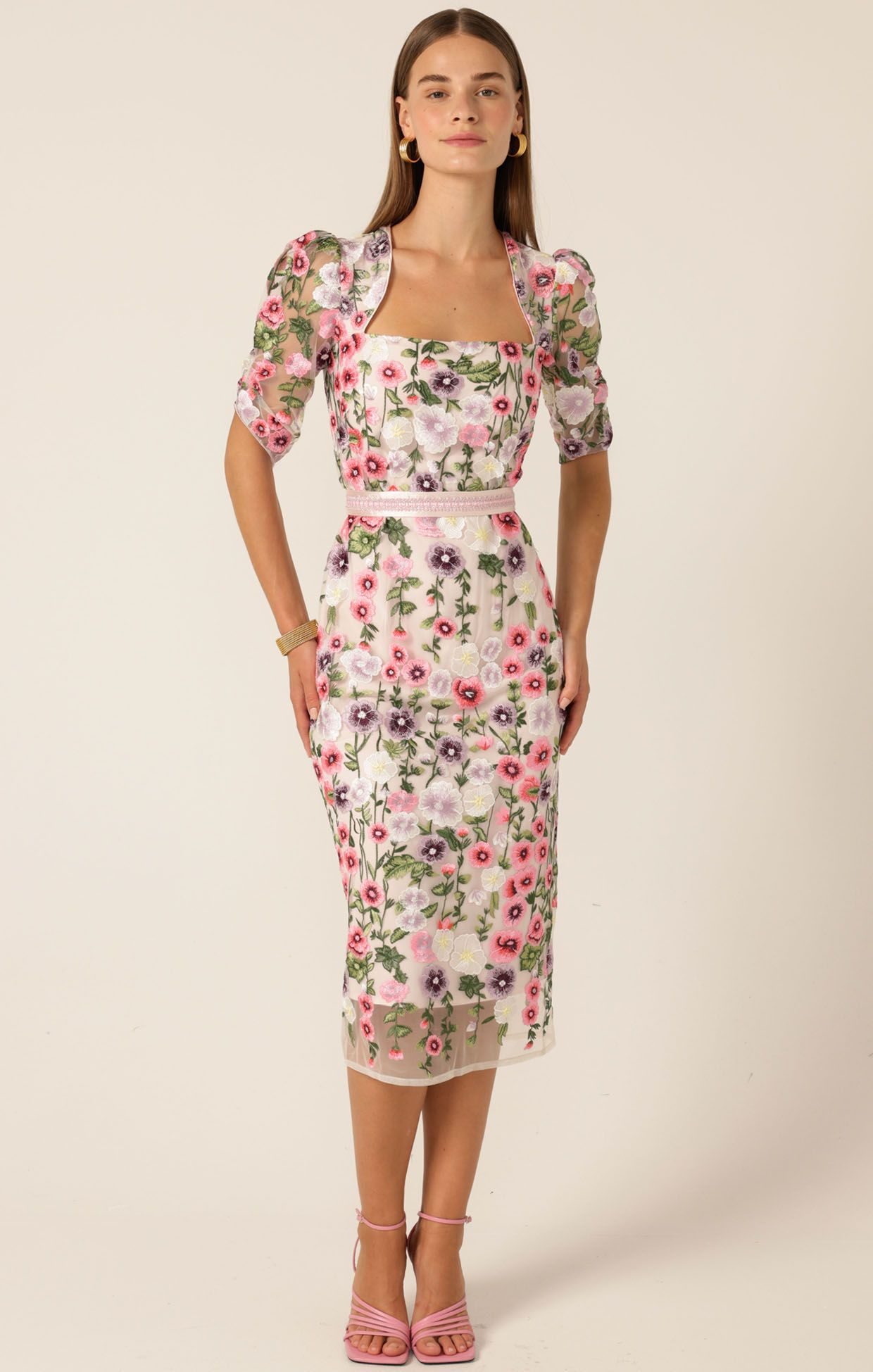 Woman in a white floral embroidered dress with puff sleeves and pink heels.