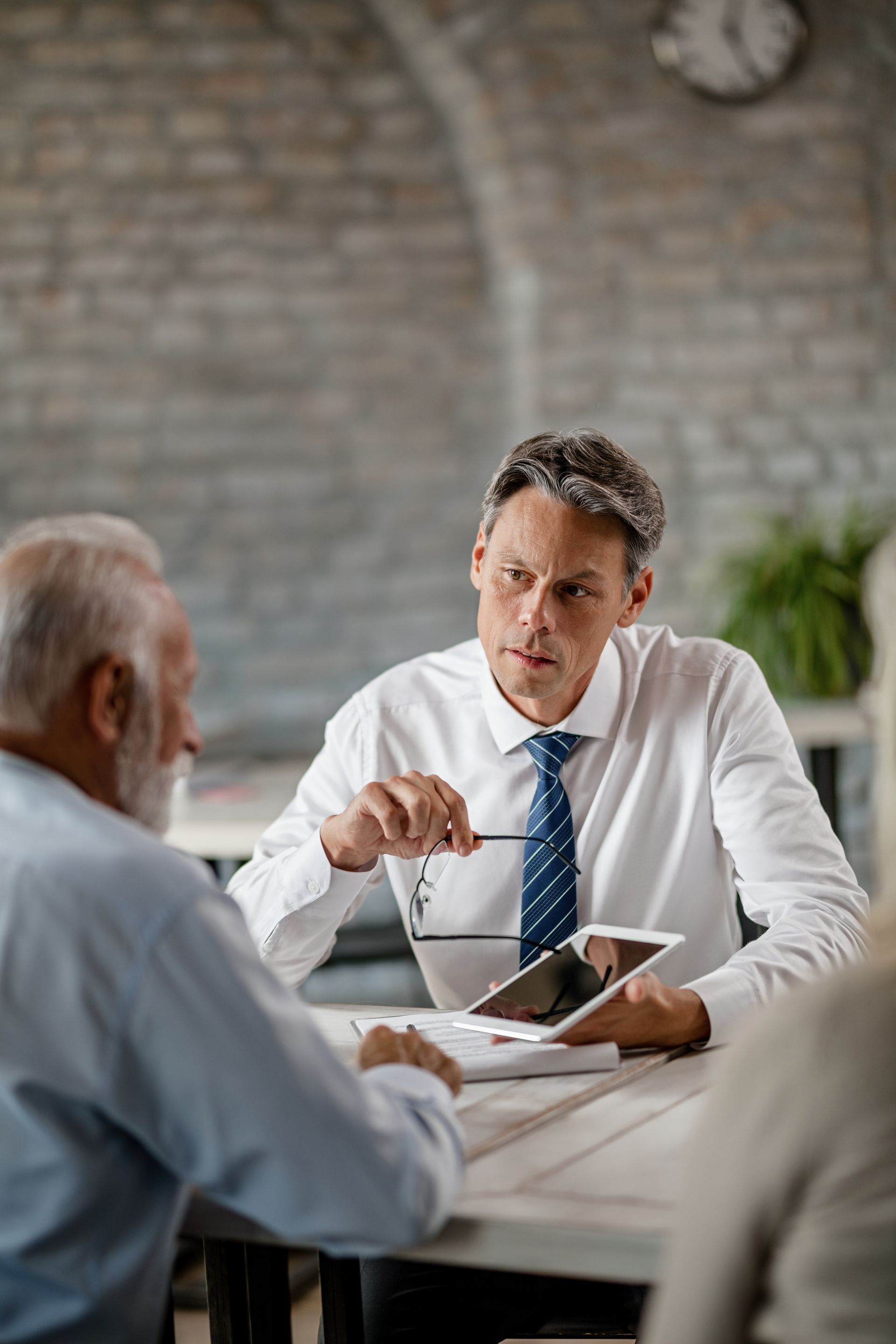 Man in white shirt explains documents to senior couple at a table.