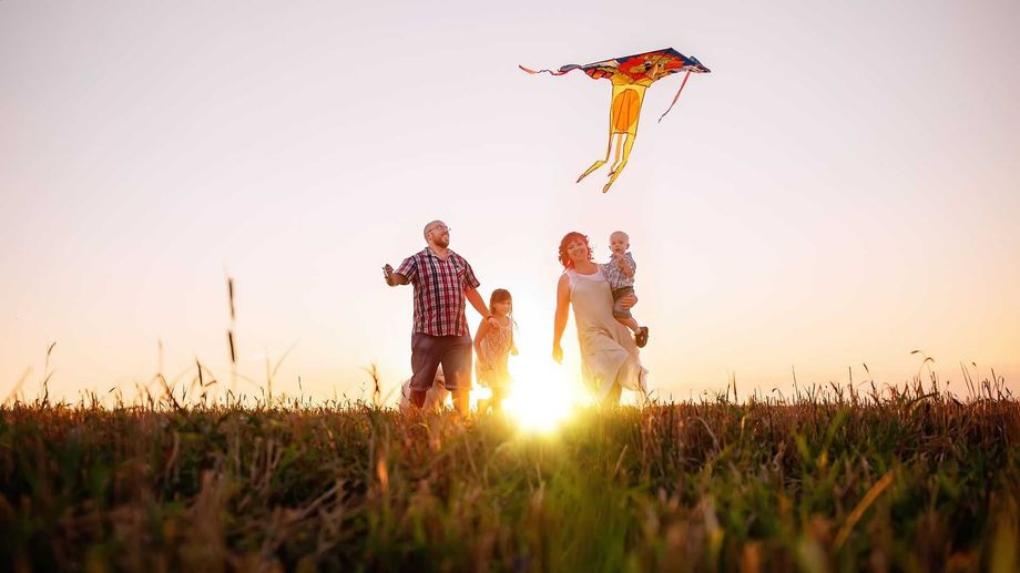 Family flying a kite at sunset in a field. Kite is orange and blue.