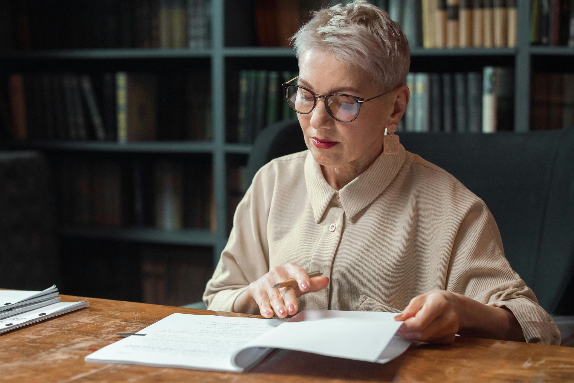 Person reading papers at a desk in a library, with shelves in the background