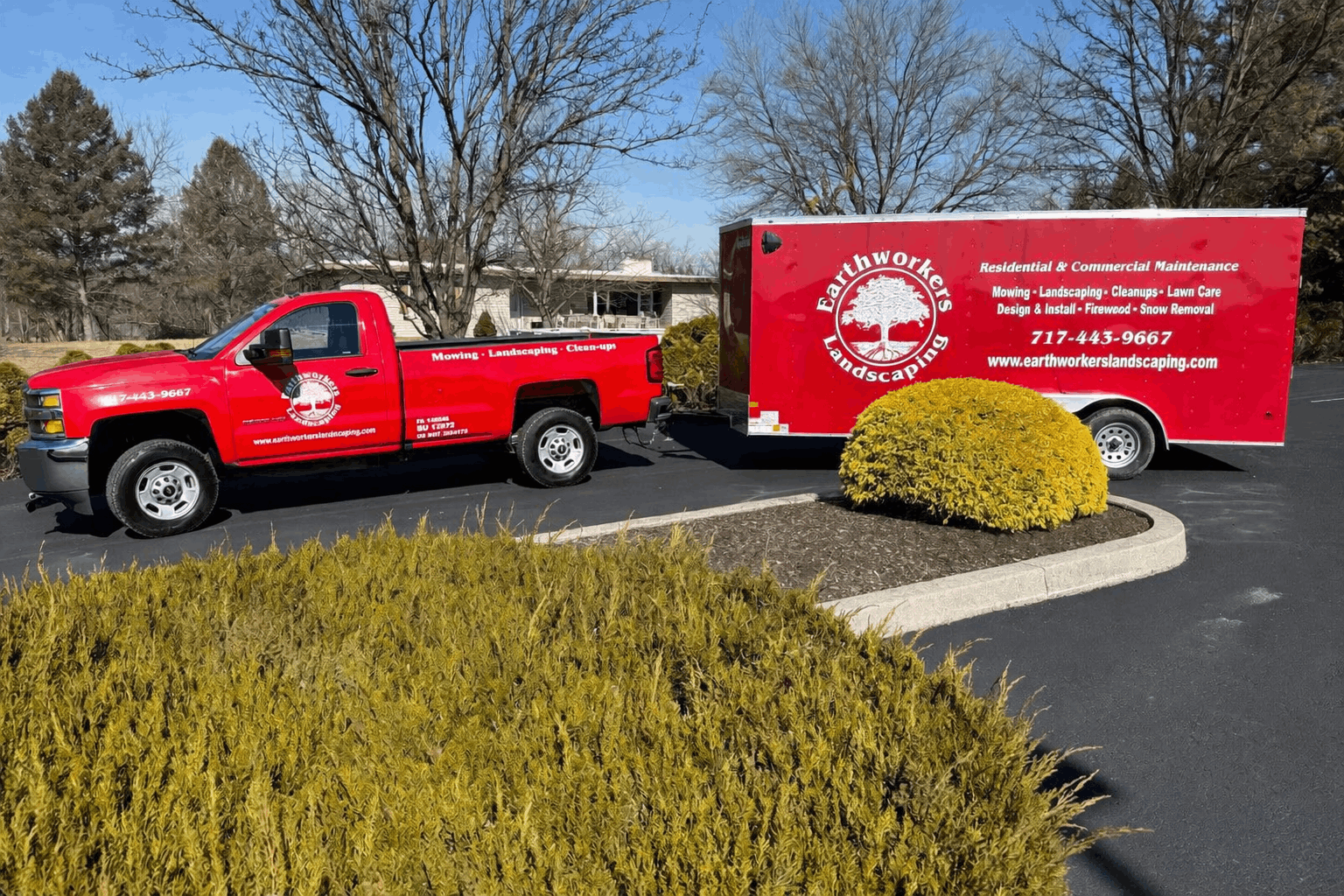 A red truck is pulling a white trailer in a parking lot.