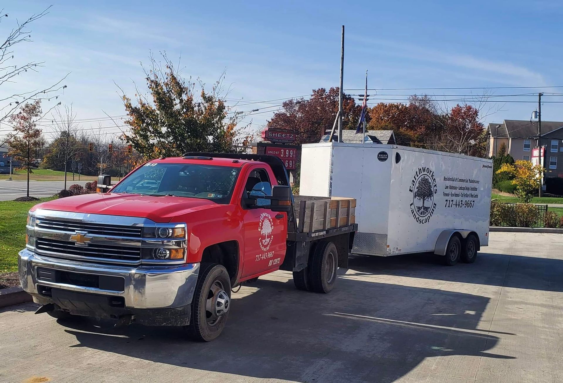 A red truck is pulling a white trailer in a parking lot.